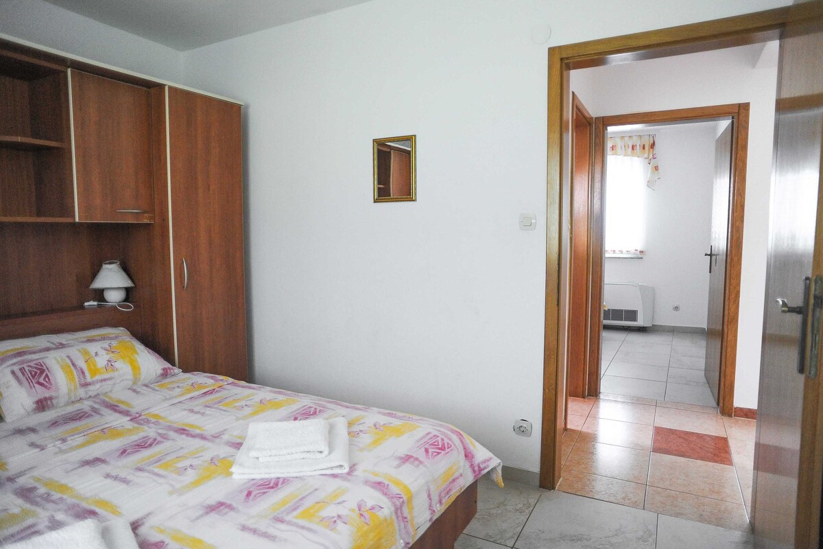A bedroom with a bed, wooden wardrobe, and a small mirror on the wall.