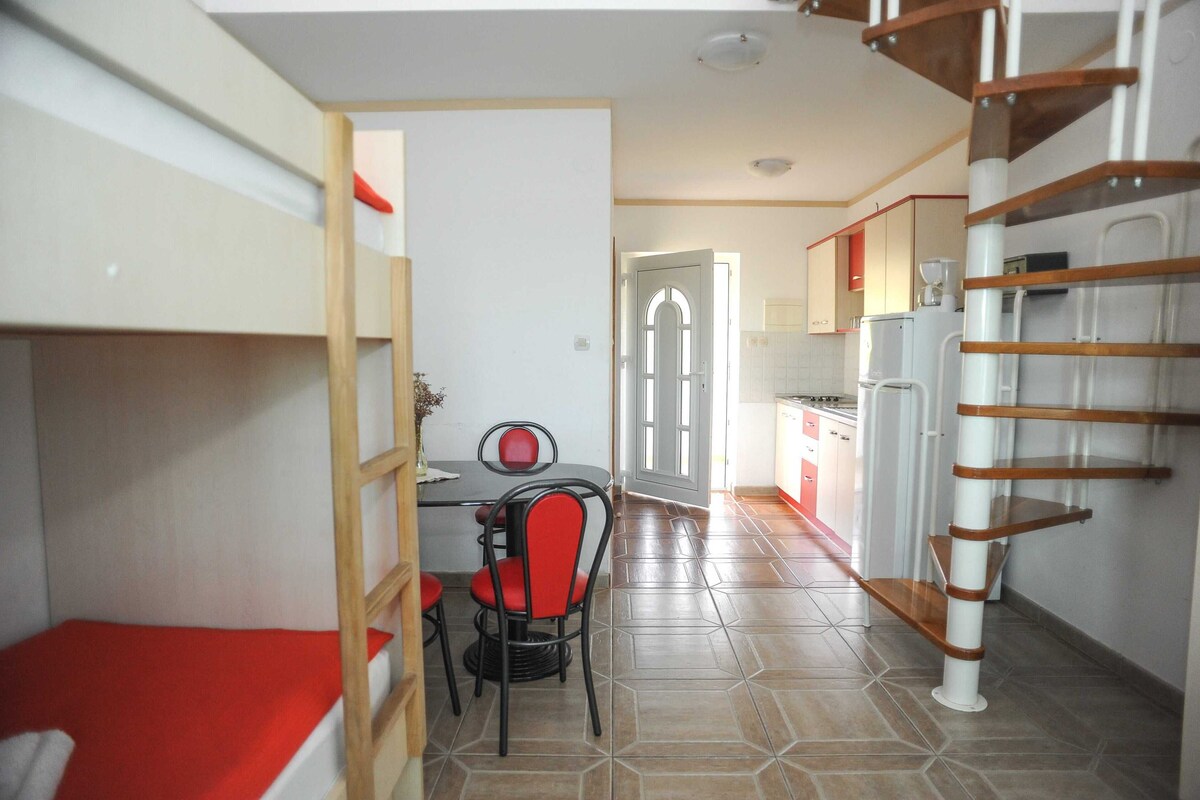 A compact kitchen with a dining area, a staircase, and a bunk bed.