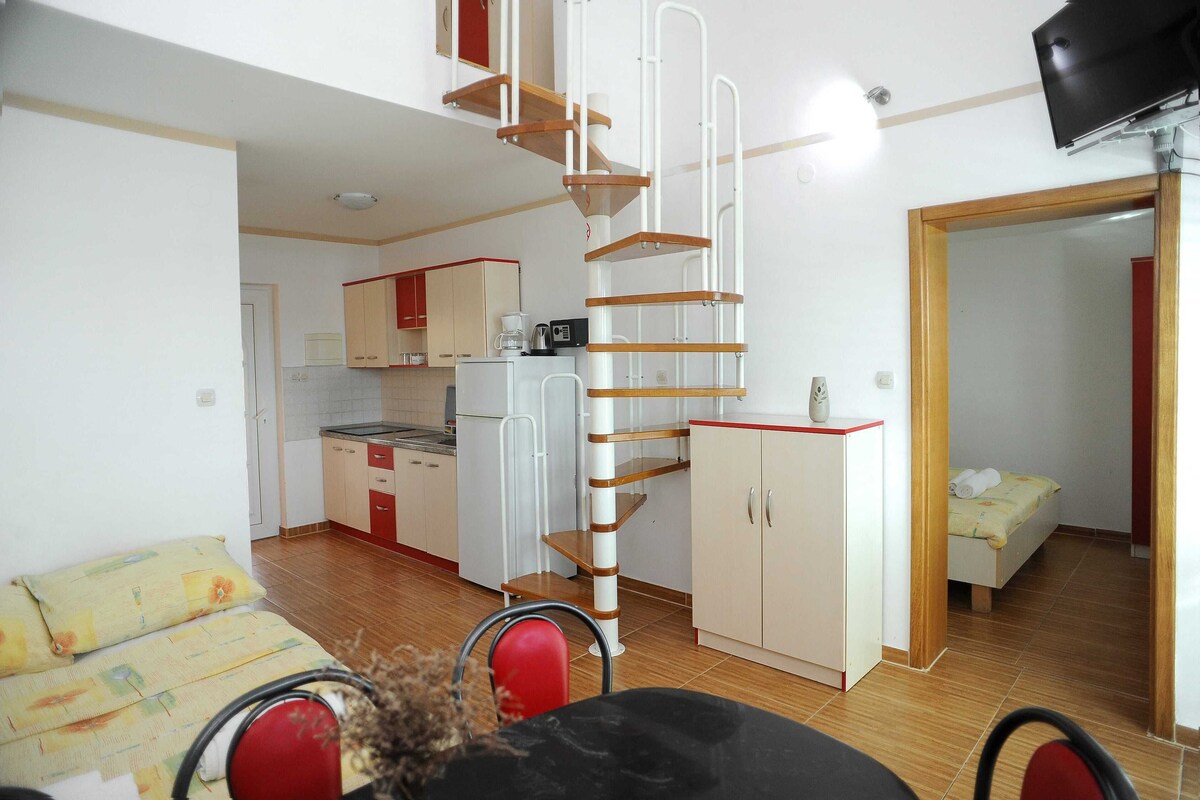 A compact living space with a kitchenette, a dining area, and a bedroom with a bed.