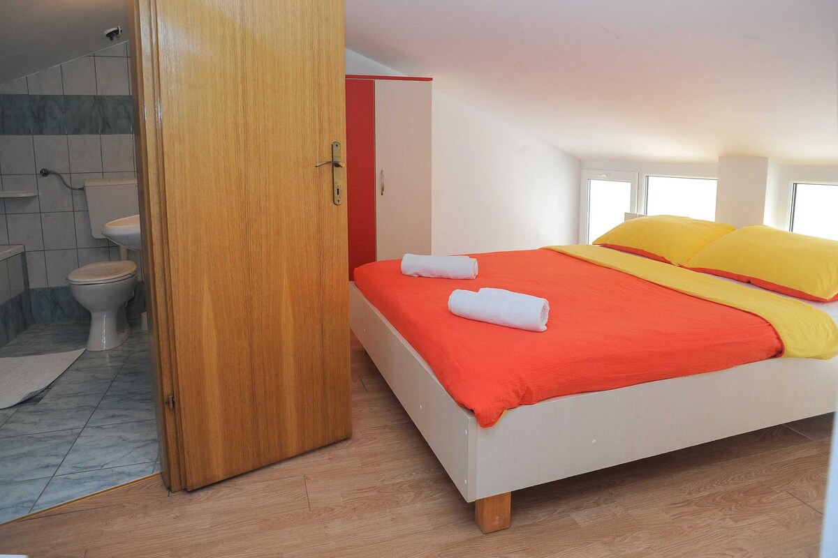 A bedroom with a bed, a bathroom with a toilet, and a wooden door.