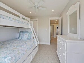 Ein Schlafzimmer mit Etagenbetten, einem Schminktisch, einem Deckenventilator und einem Flur, der in einen anderen Raum führt.