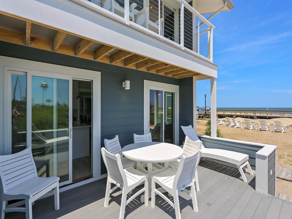 A deck with a table and chairs, overlooking a beach with lounge chairs.