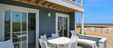 A deck with a table and chairs, overlooking a beach with lounge chairs.