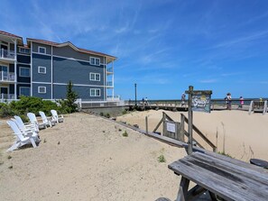 Ein Gebäude direkt am Strand mit mehreren Balkonen, einer Holzterrasse und Liegestühlen.