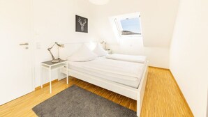 A bedroom with a bed, a bedside table with a lamp, a window with a view, and a framed picture on the wall. - Ferienresidenz Hinterzarten FEWO H9 (Hinterzarten)