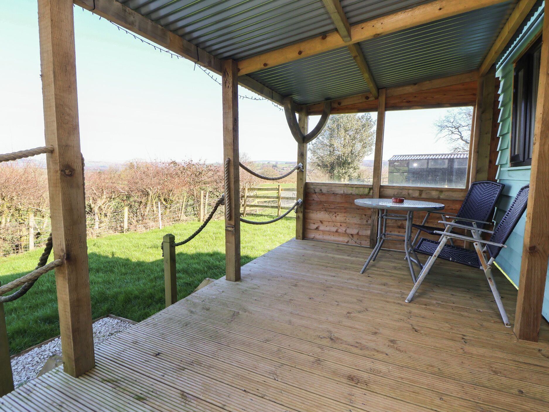 A wooden deck with a metal roof, a table, and two chairs.