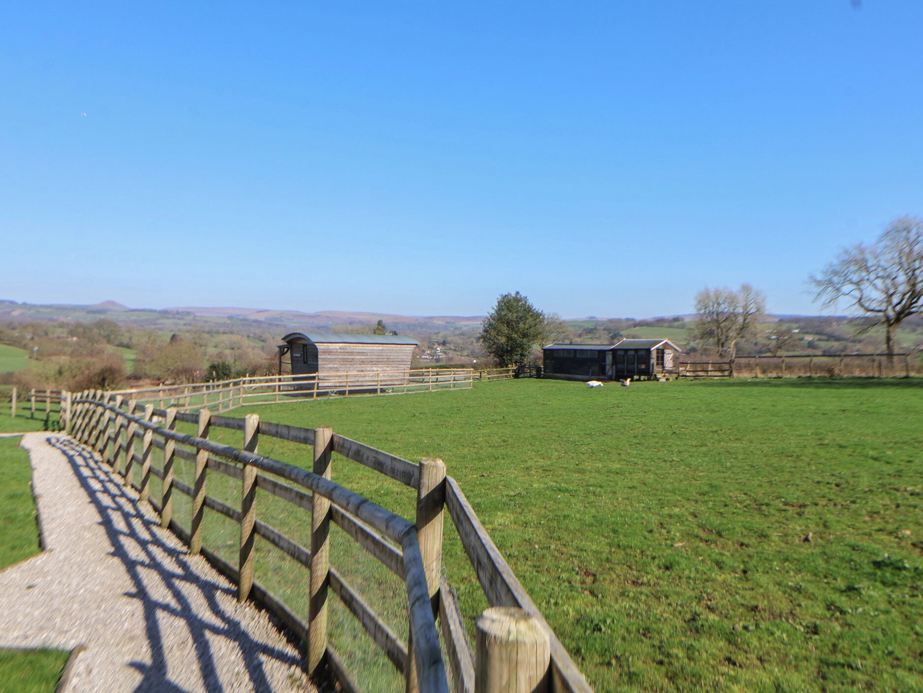 A rural landscape with a wooden fence, a small building, and a barn in the distance.
