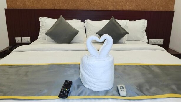 Habitación de hotel con cama, una toalla con forma de corazón y dos controles remotos sobre una manta.