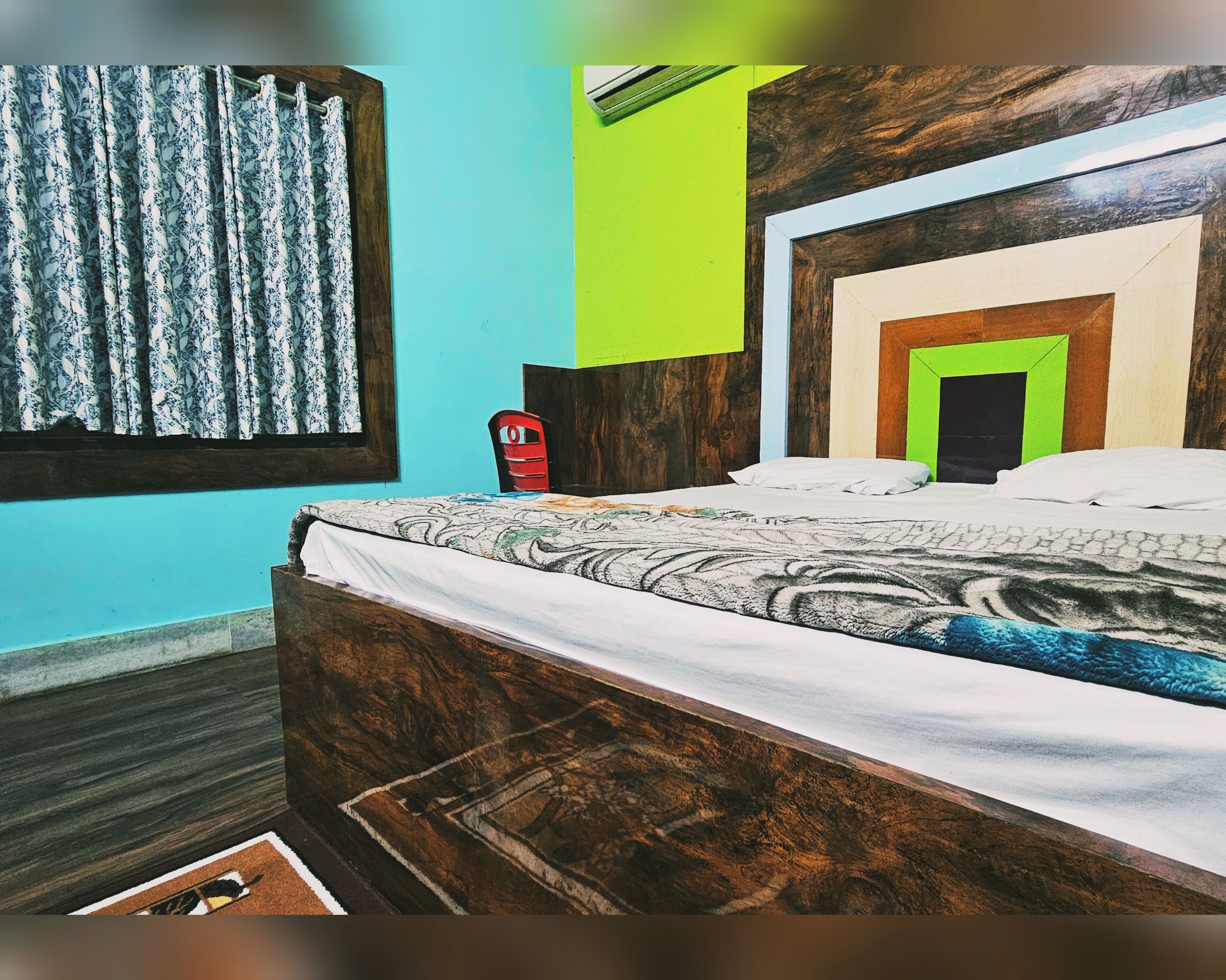 A bedroom with a wooden bed, a red chair, a window with patterned curtains, and a green wall.
