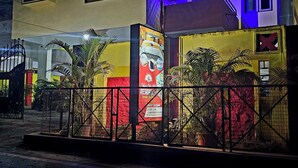 Un edificio de varios pisos con entrada protegida por una reja, que presenta un mural colorido y plantas en macetas.