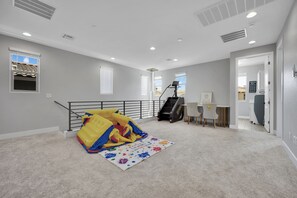 Een ruime kamer met een groot raam, een speelruimte met een kleurrijk speeksel, een bureau met een stoel, en een trap die naar een ander niveau leidt.
