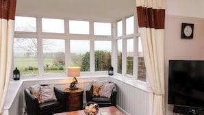 A cozy living room with a large window, a wooden coffee table, two black sofas, a television, and a decorative lamp. - Dilston House (Whitby)