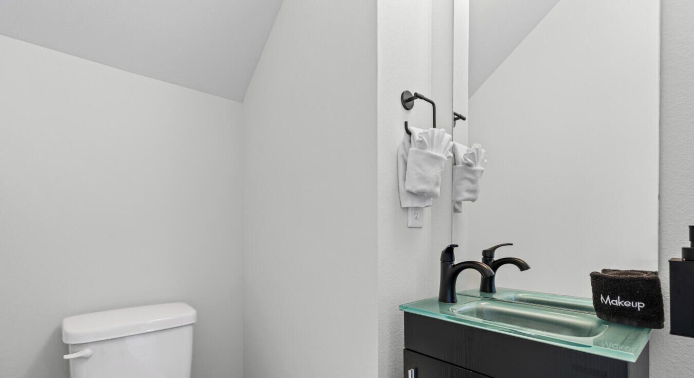 A modern bathroom with a white toilet, a glass sink with black faucets, and a mirror reflecting the room.