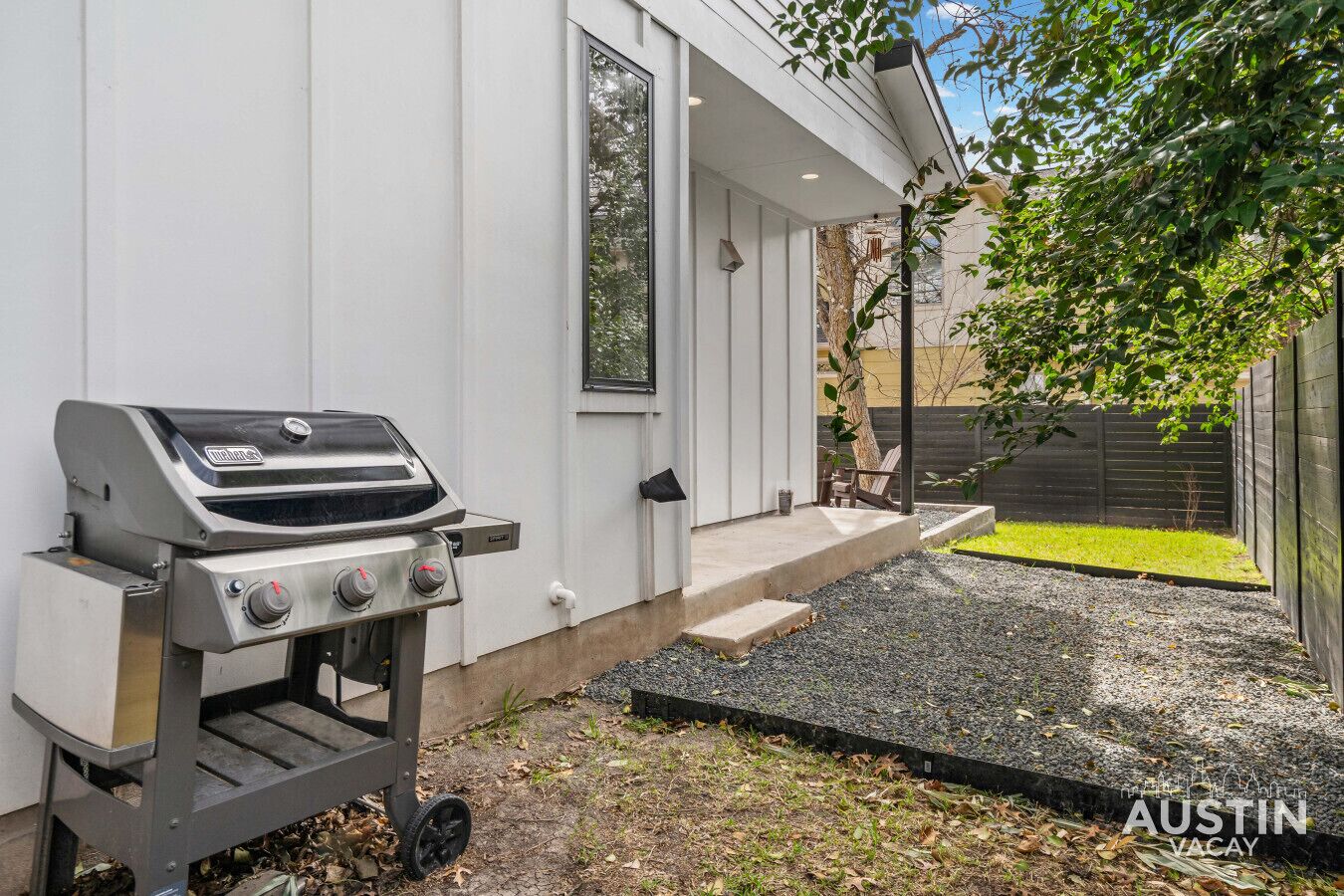 A modern outdoor grill area adjacent to a house with a concrete patio and a small garden.