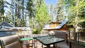 A deck with a glass-top table and chairs, surrounded by a wooden fence and tall trees. - The Cozy Moonridge Cabin (Big Bear Lake)