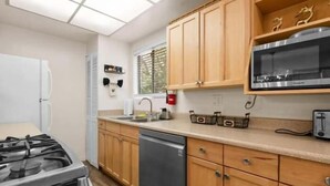 A compact kitchen with wooden cabinets, a built-in microwave, a gas stove, and a dishwasher. - The Cozy Moonridge Cabin (Big Bear Lake)