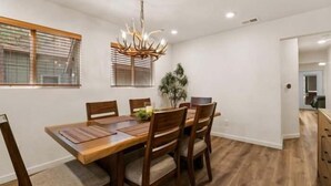 A dining room with a wooden table and chairs, a chandelier, and a window with blinds. - The Cozy Moonridge Cabin (Big Bear Lake)