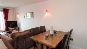 Una sala de estar con un sofá marrón, una mesa de comedor de madera con sillas, un televisor y un cuadro en la pared.