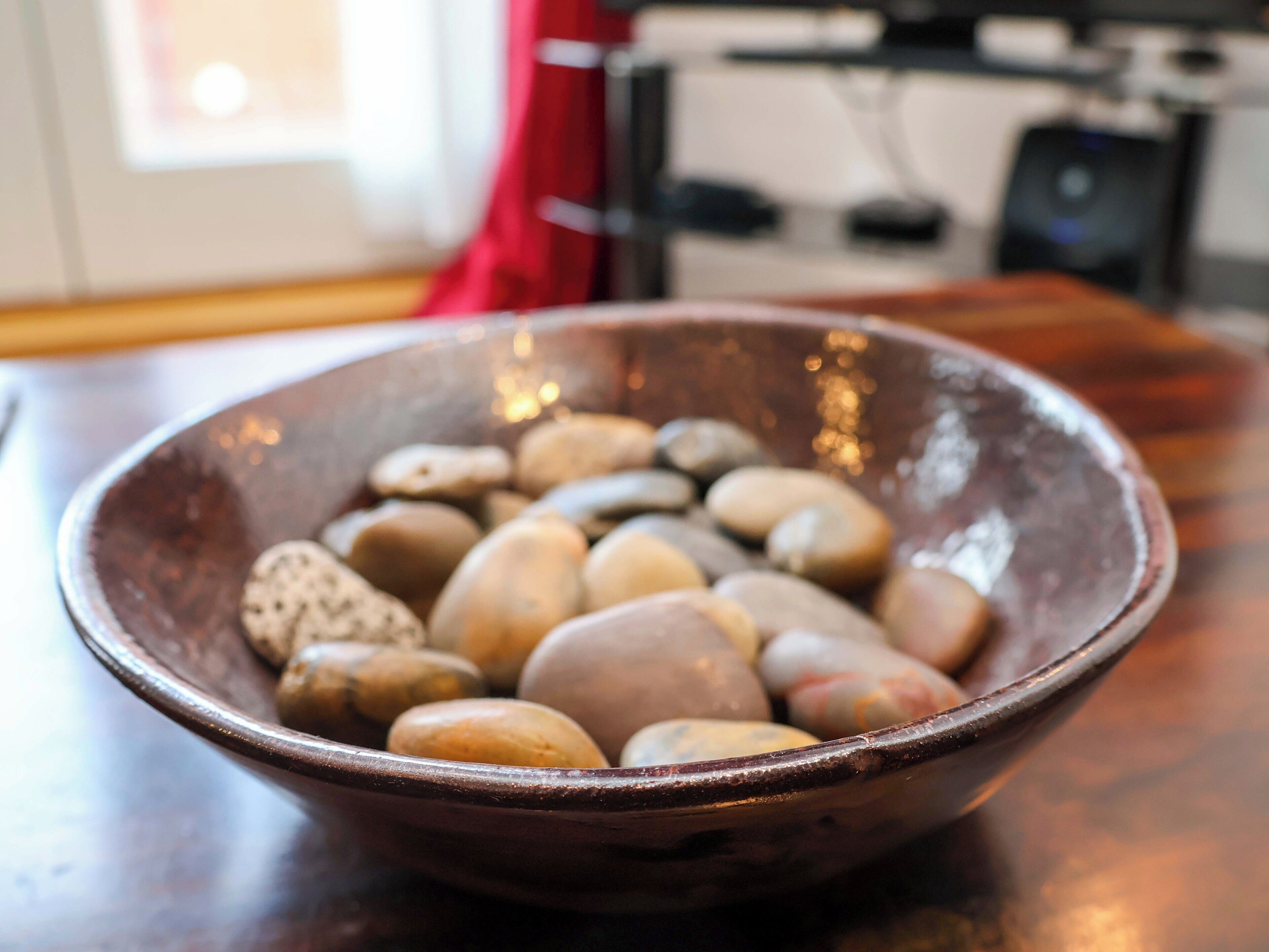 A ceramic bowl filled with smooth, rounded stones on a wooden surface.