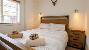 Un dormitorio con una cama de madera, dos toallas enrolladas, una cabeza de venado montada y una mesita de noche con cajones.