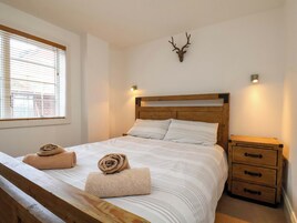 Un dormitorio con una cama de madera, dos toallas enrolladas, una cabeza de venado montada y una mesita de noche con cajones.