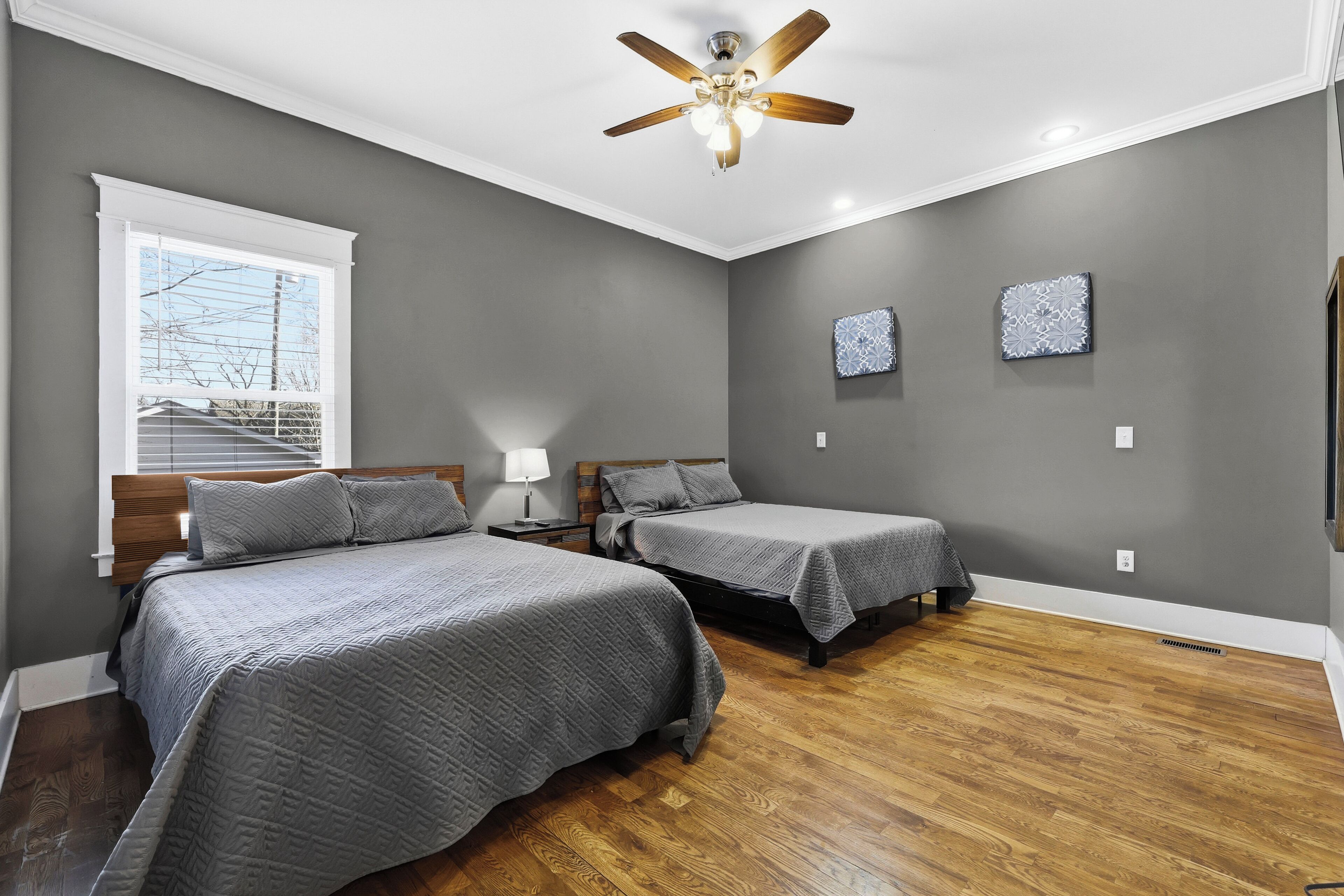 A bedroom with two beds, a ceiling fan, and a window with blinds.