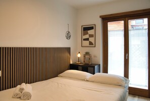 Ein Hotelzimmer mit einem Bett, einem Nachttisch mit Lampe, einem Wandbild und einem Fenster mit Jalousien.