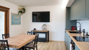 Een moderne keuken met een houten eettafel, stoelen, een televisie boven de aanrecht en een klein plankje met planten.