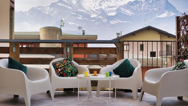 Een terras met witte stoelen en een tafel, een houten hek en uitzicht op een berg.