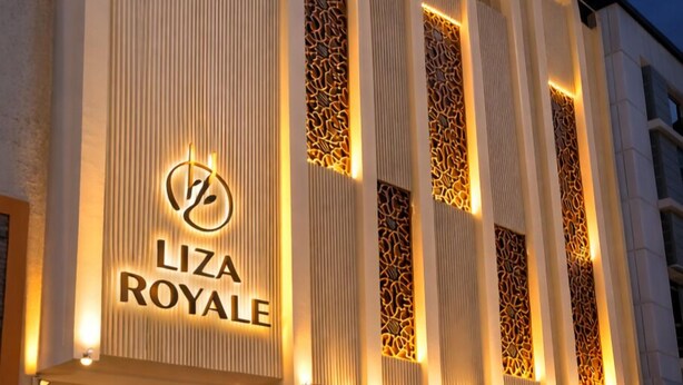 A modern building with a sign reading 'LIZA ROYALE' and a parking area with several cars.