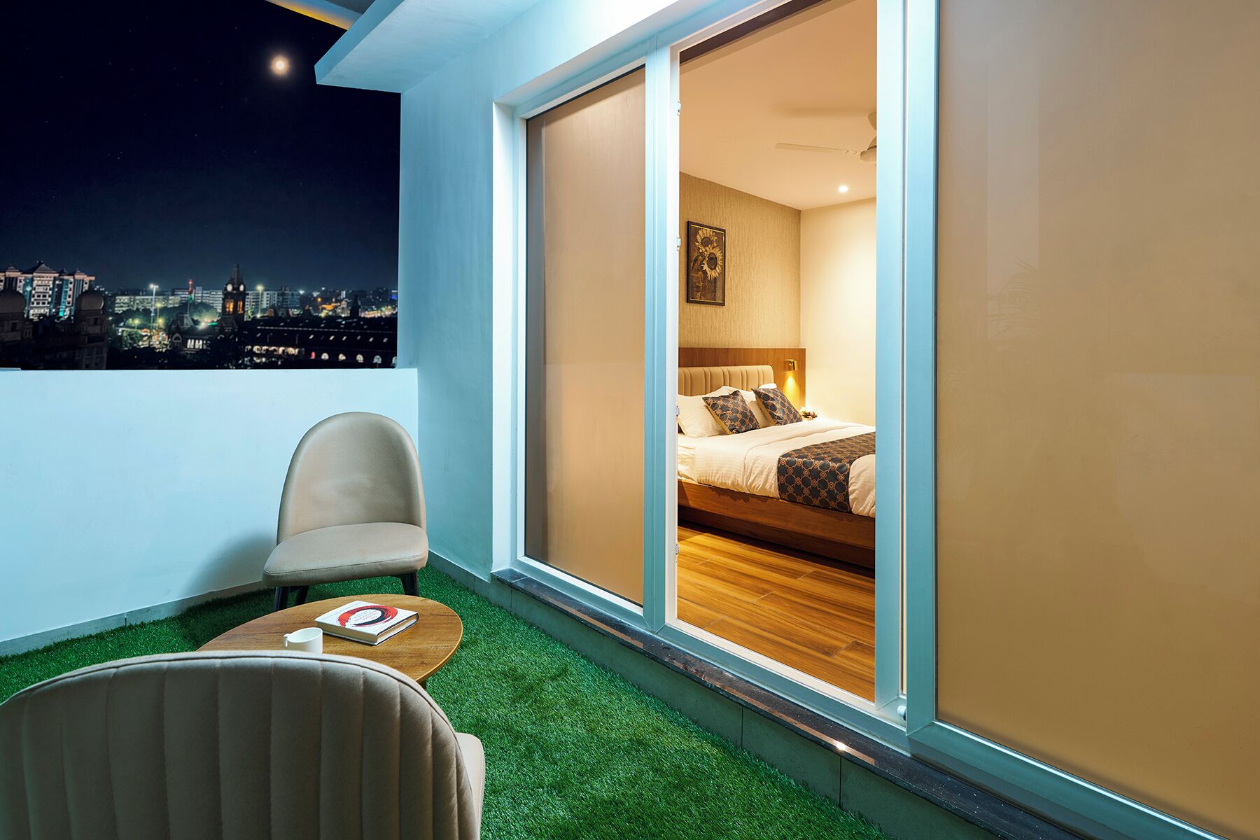 Ein modernes Hotelzimmer mit Blick auf die Stadt, inklusive Balkon mit Stuhl und Tisch sowie einer großen Schiebetür zum Schlafbereich.
