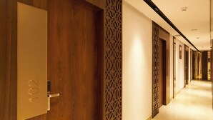 A hotel corridor with wooden doors, decorative panels, and a well-lit, tiled floor. - Liza Royale Hotel  (Chennai)