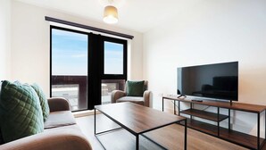 Ein modernes Wohnzimmer mit einer Couch, einem Couchtisch, einem Fernseher auf einem Holzboden und einer Schiebetür aus Glas.