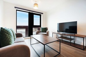 A modern living room with a sofa, a coffee table, a TV on a wooden stand, and a sliding glass door. - Modern 1-Bed Apartment Near Liverpool City Centre (Merseyside)