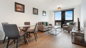 Ein modernes Wohnzimmer mit einem Glastisch, zwei Sofas, einem Fernseher auf einem Holzboden und großen Fenstern.