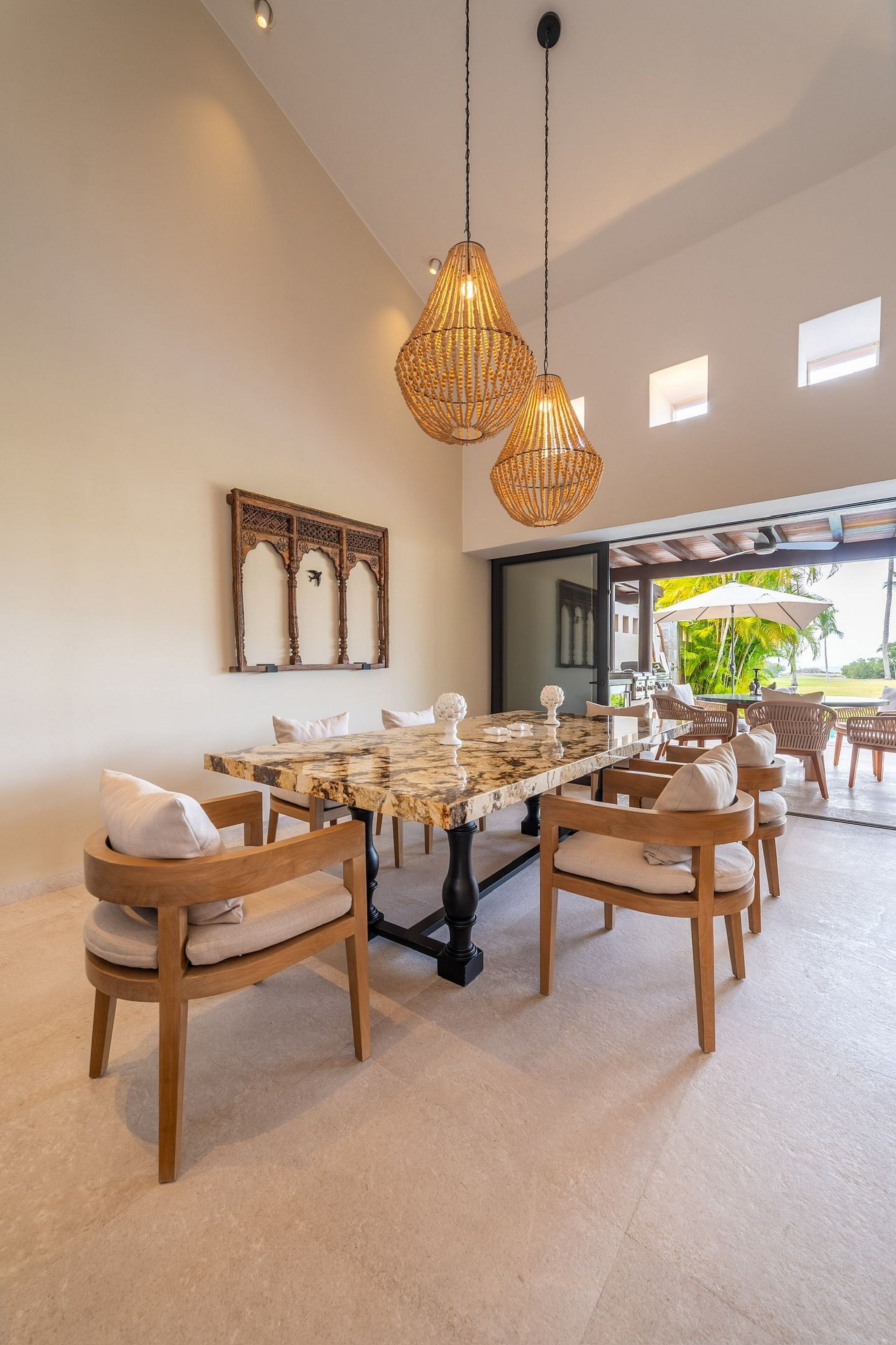 A dining area with a marble table, wicker chairs, and hanging light fixtures.