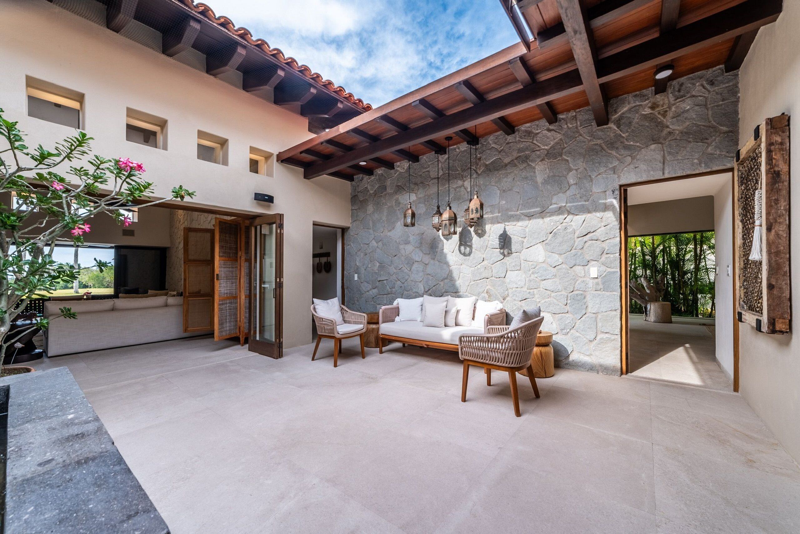 A spacious patio with a stone wall, wooden ceiling, and a sofa set.