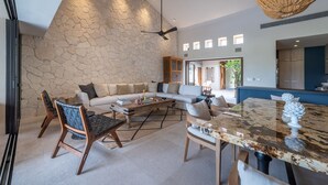 Un salón espacioso con pared de piedra, un sofá grande, una mesa de centro y un comedor con mesa de mármol.