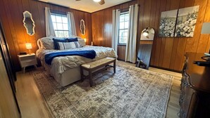 A bedroom with a bed, bedside tables, a bench, a ceiling fan, and a rug.
