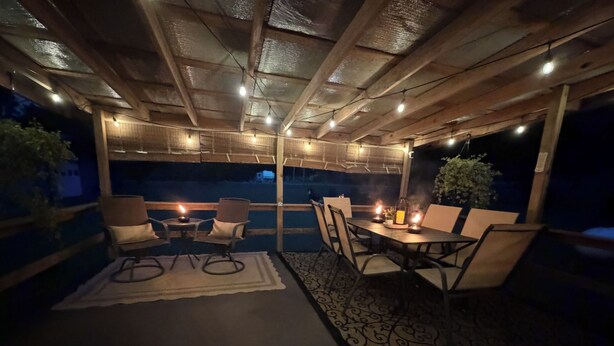 An outdoor patio with wooden furniture, string lights, and candles.