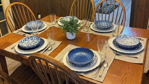A dining table with blue patterned plates, wooden chairs, a potted plant, and a wooden wall with a hanging wreath.