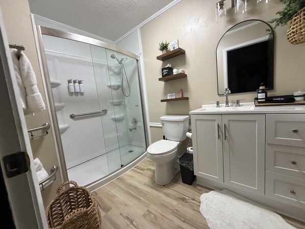 Ein Badezimmer mit Duschkabine aus Glas, Toilette, Waschbecken und Spiegel.