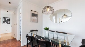 Een moderne eetruimte met een glazen tafel en zwarte stoelen, een hanglamp en een ronde spiegel aan de muur.