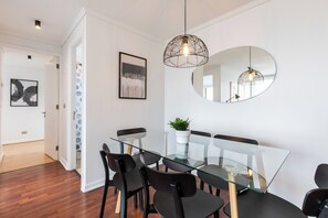 Un espace repas moderne avec une table en verre et des chaises noires, un luminaire suspendu et un miroir rond accroché au mur.