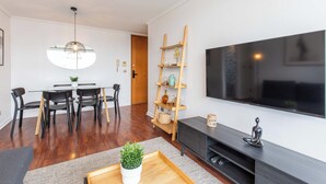 Een moderne woonkamer met een eethoek, een aan de muur bevestigde televisie en een houten laddenplank.