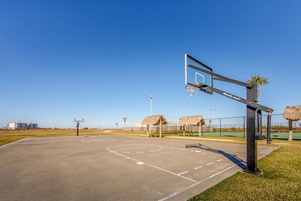 Un terrain de basket en plein air, avec un panier, un filet et un ciel dégagé.