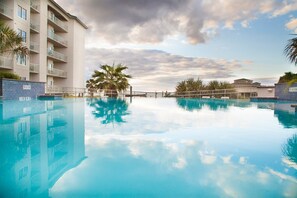 Une piscine à l’eau claire, dont la surface reflète les bâtiments environnants et les palmiers.