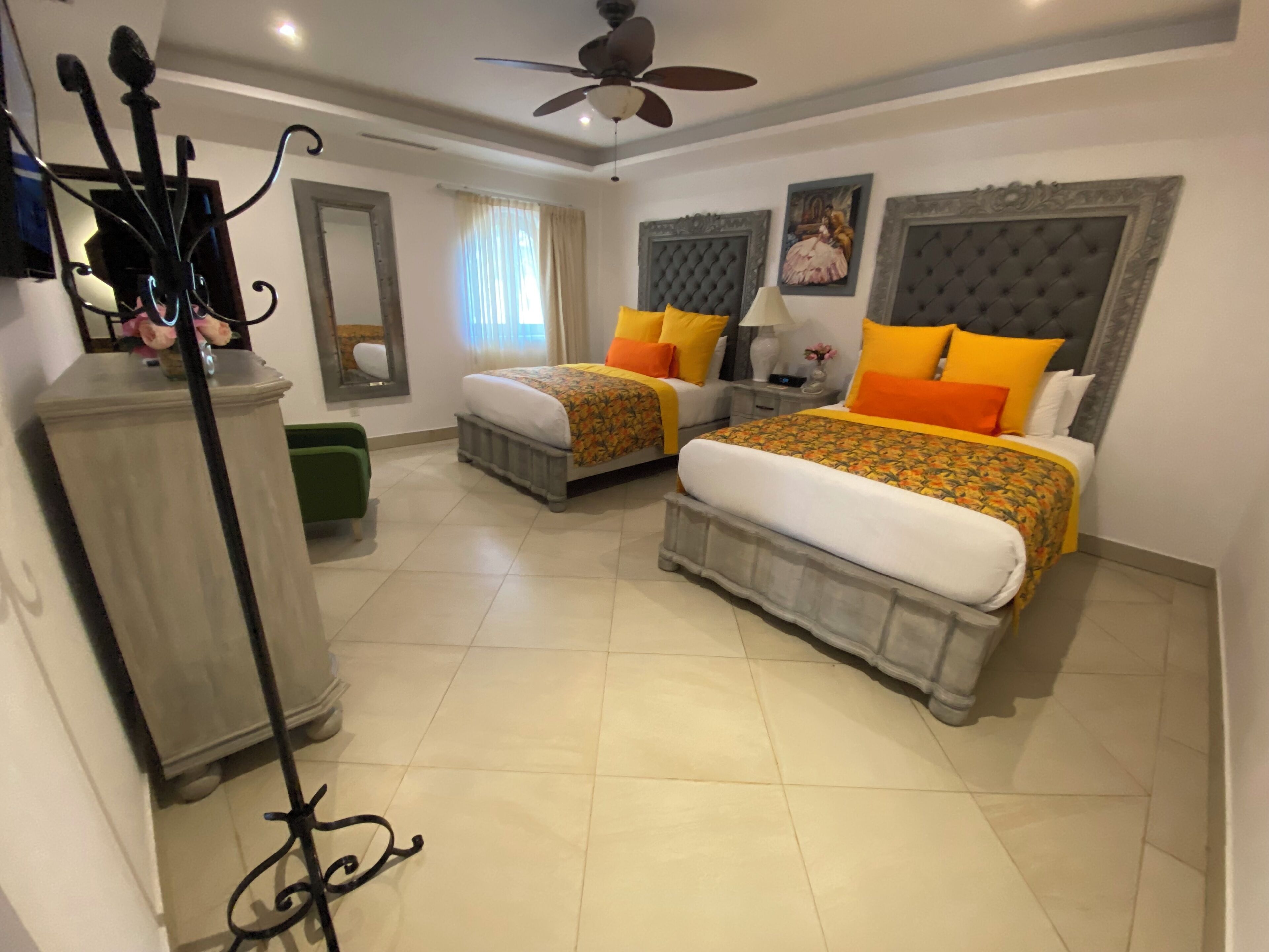 A hotel room with two beds, a ceiling fan, a green chair, and a decorative mirror.