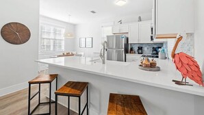 A modern kitchen with white cabinetry, a large island with stools, a stainless steel refrigerator, and a decorative flamingo sculpture. - Bikes*Pool&Hottub*Walk2Beach (Santa Rosa Beach)