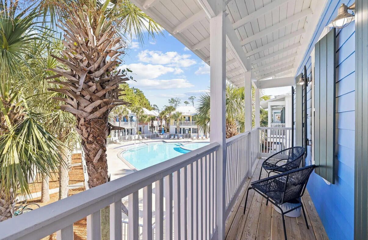 A balcony with a pool, palm trees, and a view of other buildings.